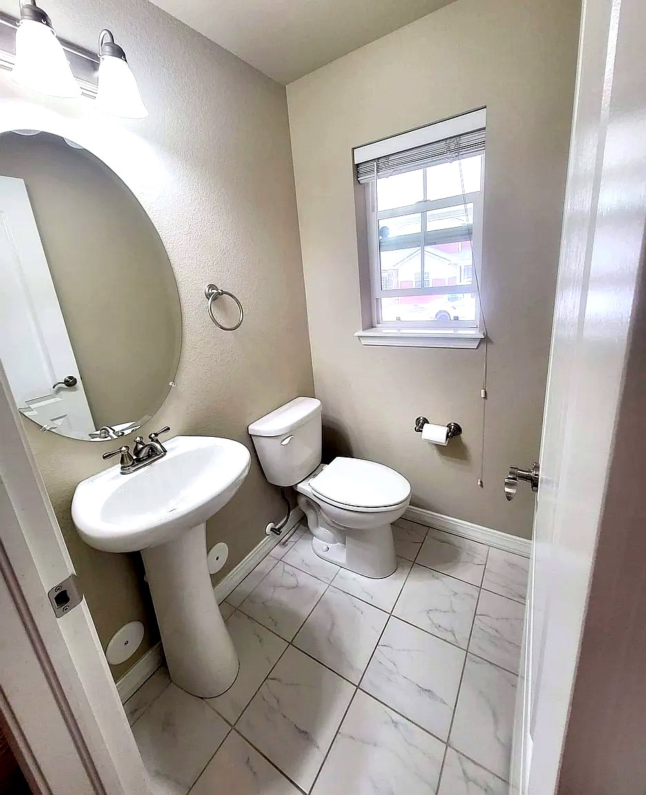 Powder room with pedestal sink, oval mirror, and marble tile floor