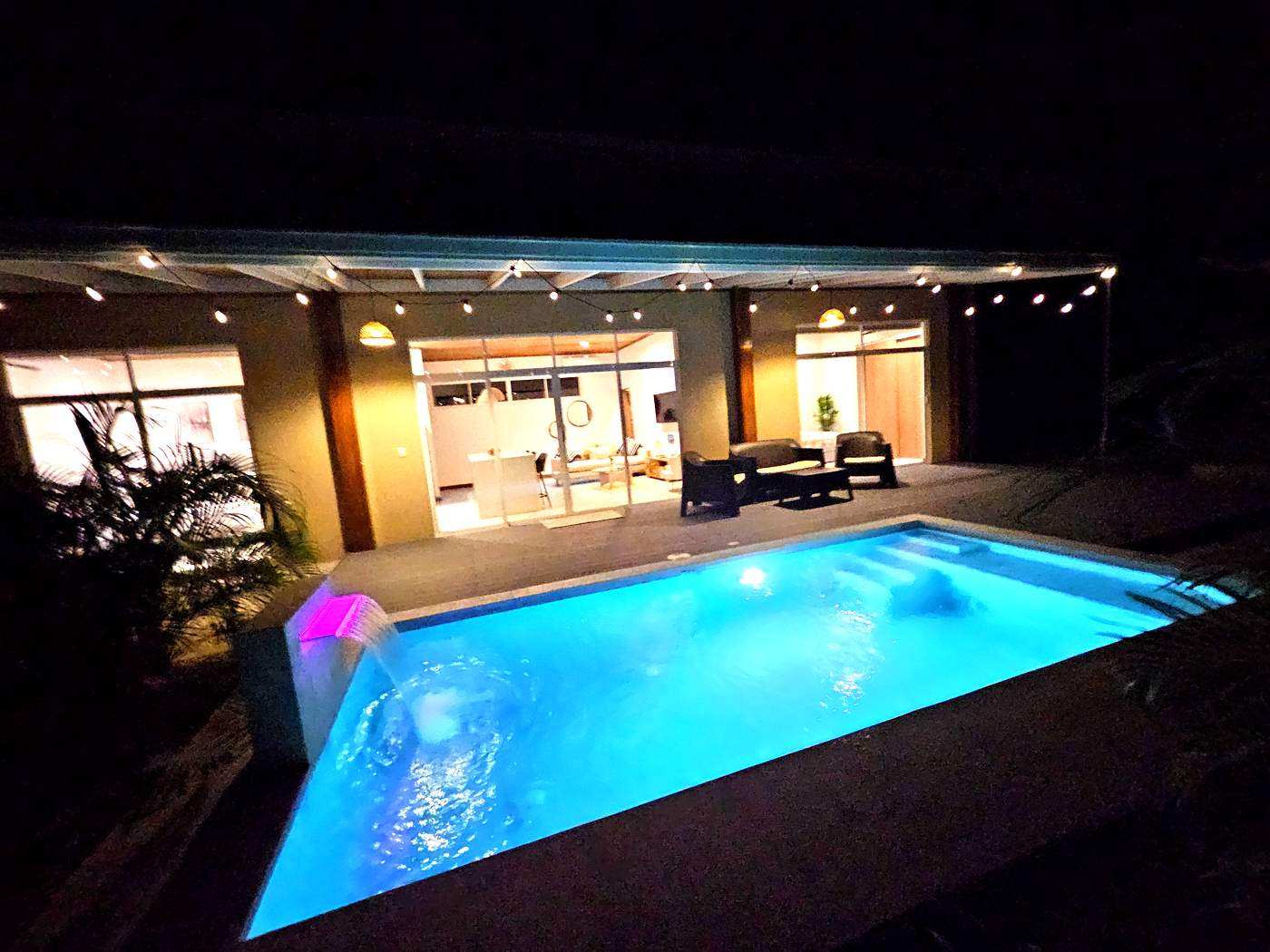 Pool at night with illuminated waterfall feature and string lights